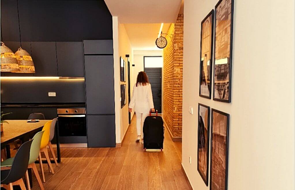 Mujer vestida de blanco con maleta dirigiéndose hacia la puerta del alojamiento